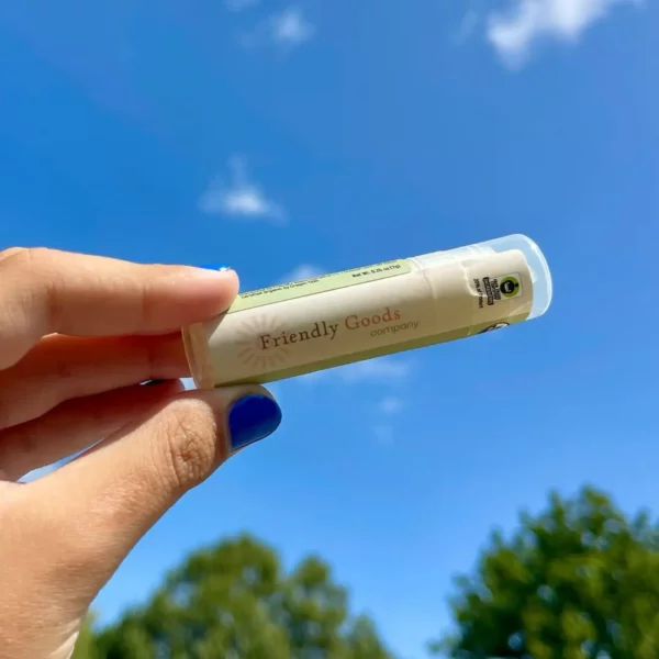 Hand holding a tube of Friendly Goods Lip Balm up to the blue sky