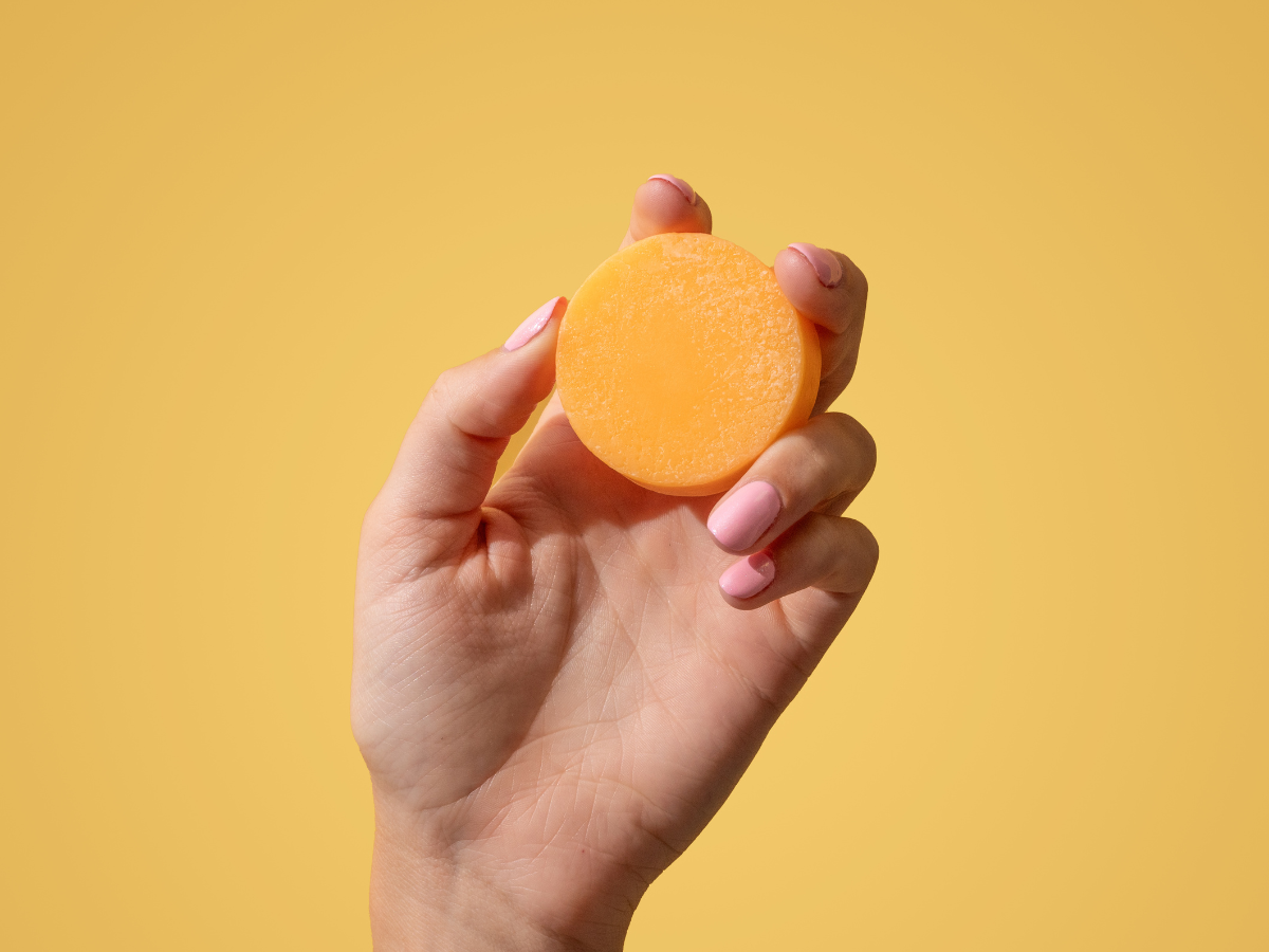 Hand holding a Friendly Goods conditioner bar on a yellow background