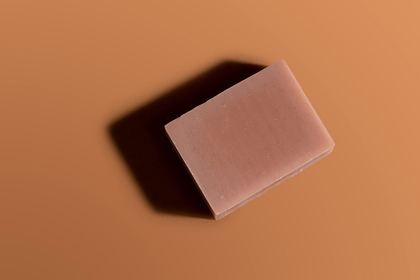 Cherry Almond Goat Milk Soap Bar, unwrapped, on a burnt orange background