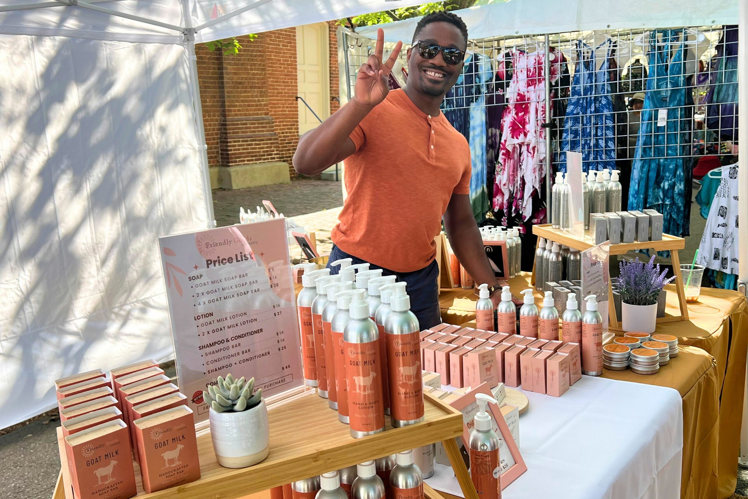 Friendly Goods Founder, Sam Shoge, giving the peace sign behind the booth at a festival in 2024