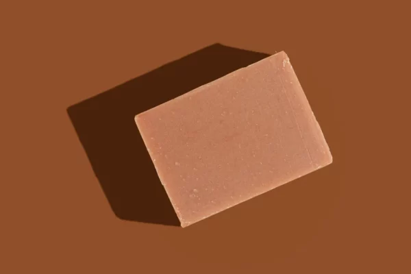 Almond & Cherry goat milk soap bar unwrapped on a dark brown background