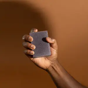 Black hand gripping Lavendar & Sage soap bar against a brown backdrop