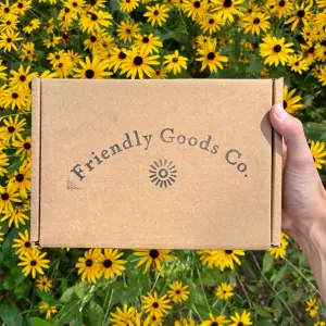 Friendly Goods product box being held over a bed of Maryland flower, black eyed susans