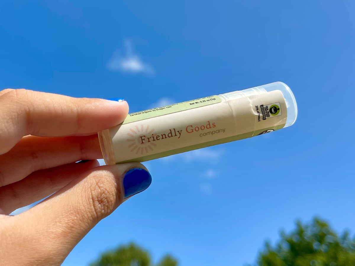 Horizontal Image of Friendly Goods Lip Balm held between forefinger and thumb facing up against a blue sky