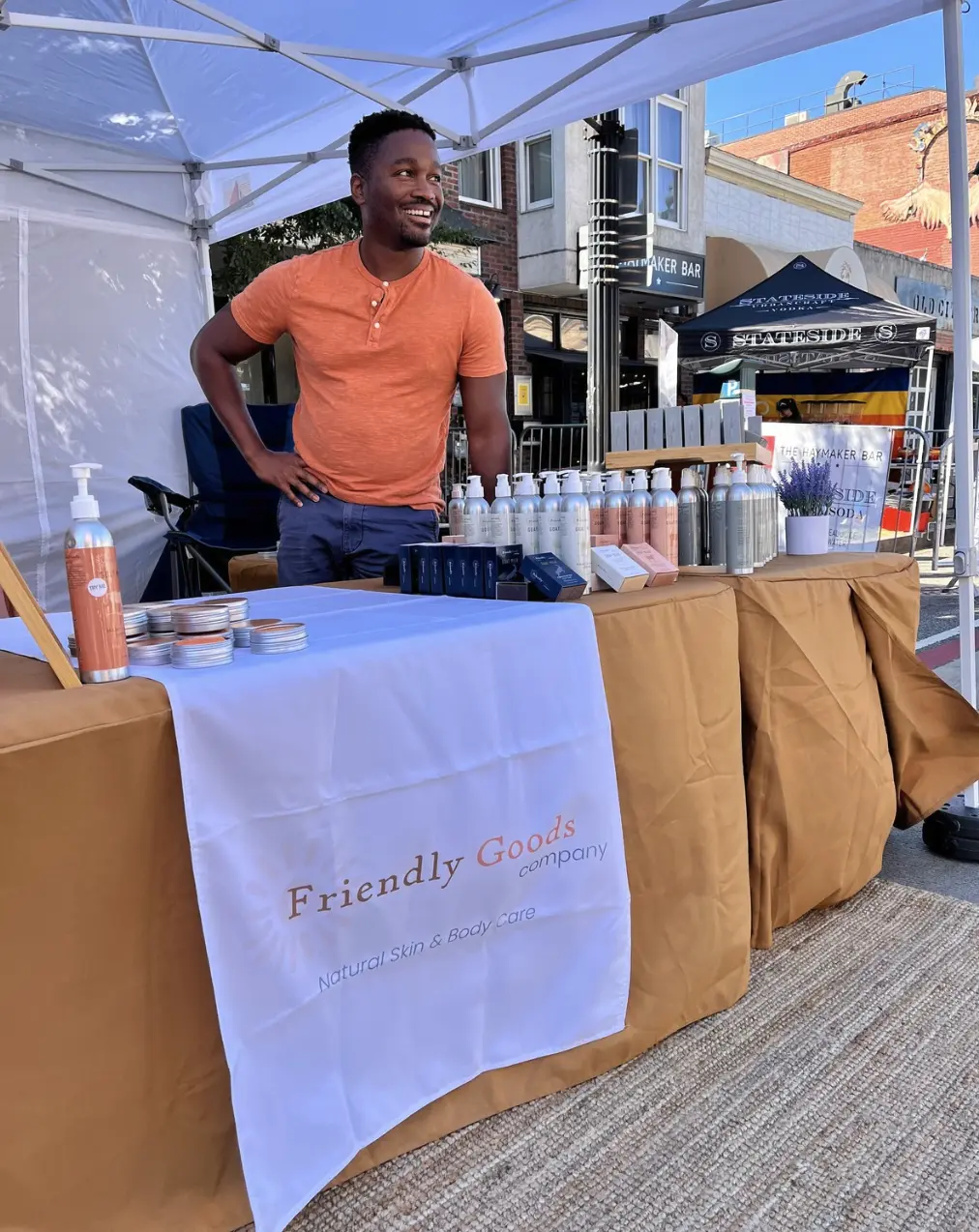 Founder, Sam Shoge smiling away from the camera as he stands behind the Friendly Goods market booth