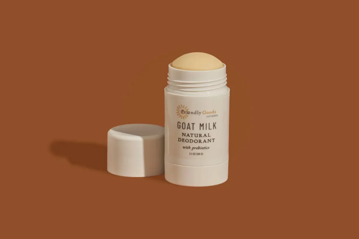 Friendly Goods Natural goat milk deodorant open with cap beside it against a brown background